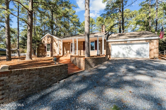 ranch-style house with brick siding, a chimney, covered porch, an attached garage, and driveway