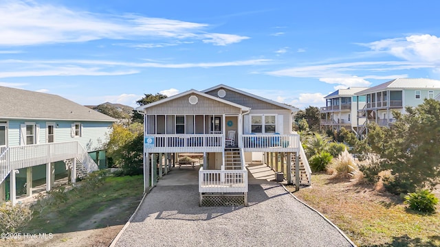 beach home with a carport, gravel driveway, covered porch, and stairway