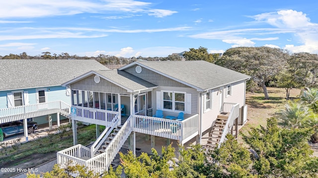 rear view of property with a sunroom, roof with shingles, and stairs