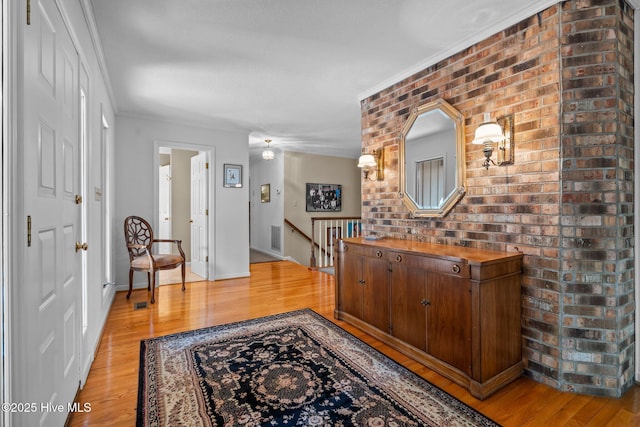 foyer entrance with light wood-style floors, brick wall, and crown molding