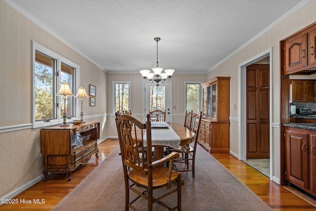 dining room with wallpapered walls, a textured ceiling, wood finished floors, and an inviting chandelier