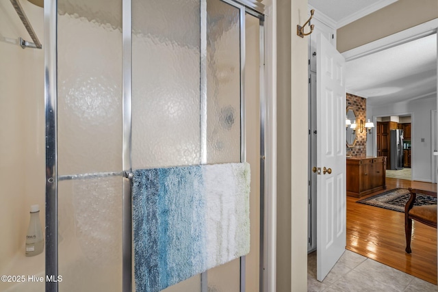 full bathroom with tile patterned flooring, crown molding, and a shower stall