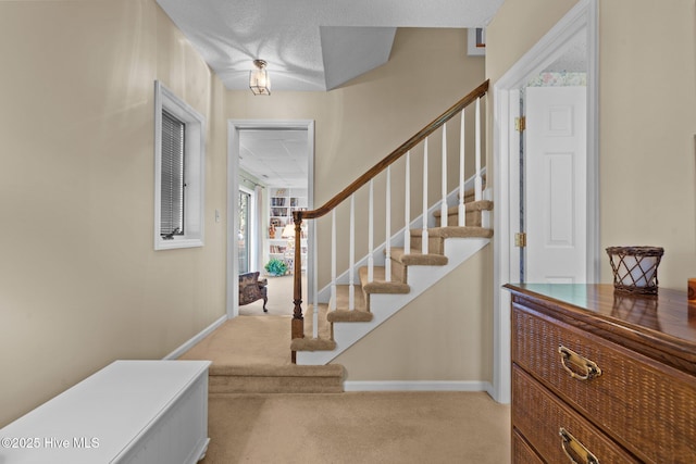 entrance foyer with light colored carpet, stairway, and baseboards