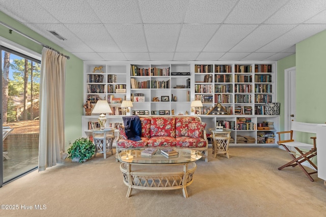 living area with carpet floors, visible vents, a drop ceiling, and bookshelves