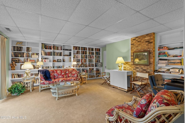 living area featuring wall of books, carpet, visible vents, and a drop ceiling