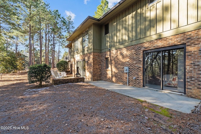 exterior space featuring board and batten siding, brick siding, and a patio