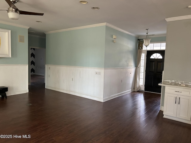 entryway with ornamental molding, dark wood finished floors, a ceiling fan, and wainscoting