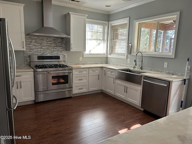 kitchen with crown molding, wall chimney range hood, appliances with stainless steel finishes, and white cabinetry