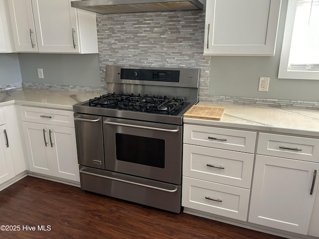 kitchen featuring range with two ovens, light stone counters, white cabinets, wall chimney range hood, and decorative backsplash