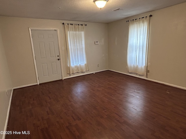 empty room featuring dark wood-style flooring, visible vents, a textured ceiling, and baseboards