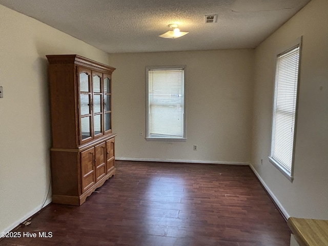 unfurnished dining area featuring dark wood-type flooring, visible vents, a textured ceiling, and baseboards