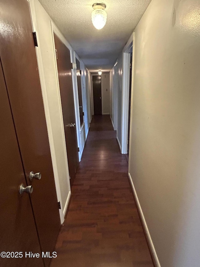 corridor featuring dark wood-style floors, a textured ceiling, and baseboards