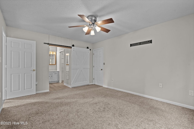 unfurnished bedroom with a textured ceiling, connected bathroom, ceiling fan, a barn door, and light colored carpet