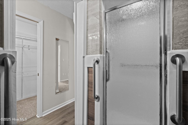 bathroom with wood-type flooring, a shower with door, and a textured ceiling