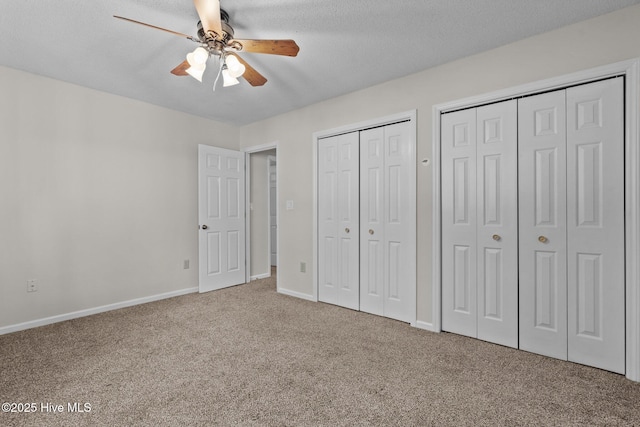 unfurnished bedroom featuring ceiling fan, multiple closets, carpet, and a textured ceiling