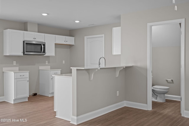 kitchen featuring a peninsula, light wood-style floors, a breakfast bar area, white cabinetry, and stainless steel microwave