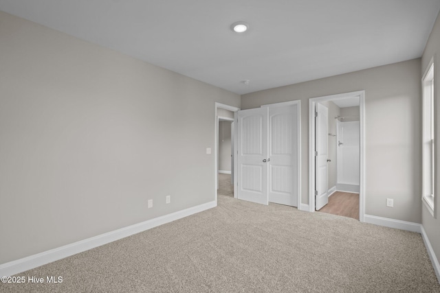 unfurnished bedroom with baseboards, ensuite bathroom, and carpet