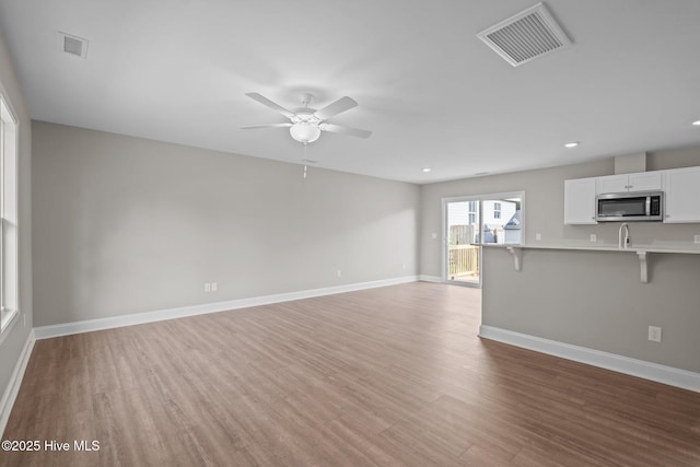 unfurnished living room with a ceiling fan, baseboards, visible vents, and light wood-style flooring