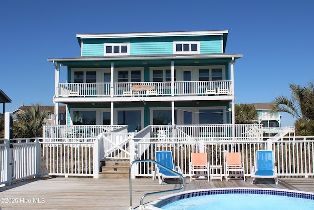 rear view of house featuring fence, a wooden deck, a balcony, and an outdoor pool