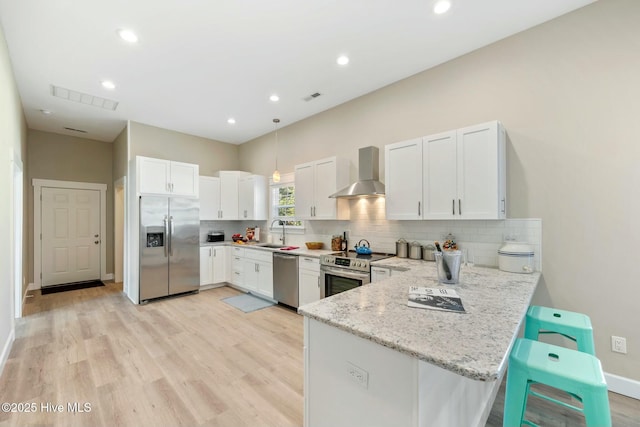 kitchen featuring wall chimney range hood, white cabinetry, appliances with stainless steel finishes, and a sink