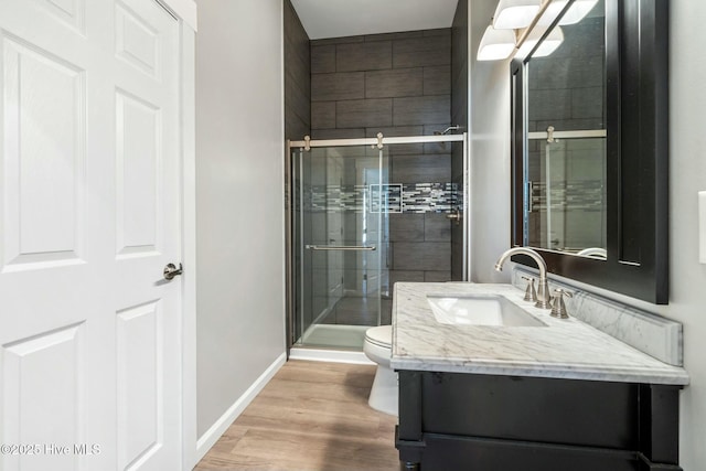 full bathroom featuring toilet, wood finished floors, vanity, baseboards, and a stall shower