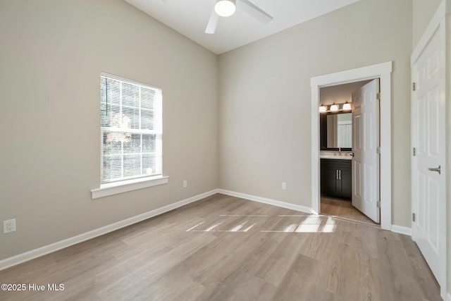 unfurnished bedroom featuring light wood-style floors, baseboards, a sink, and ensuite bathroom