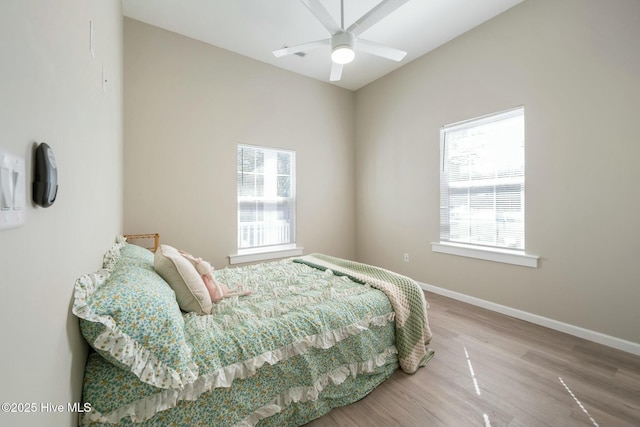 bedroom with multiple windows, wood finished floors, a ceiling fan, and baseboards