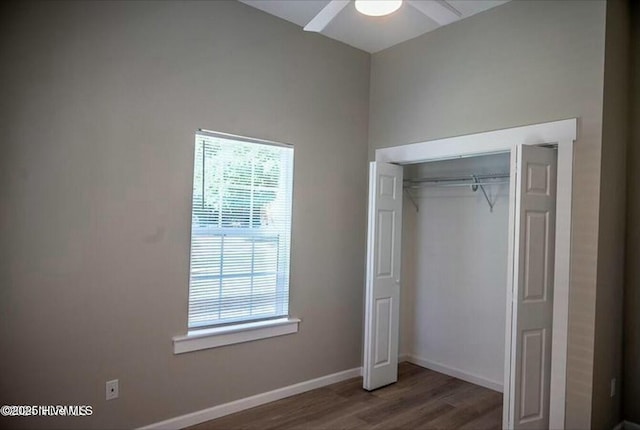 unfurnished bedroom featuring dark wood-style floors, a closet, multiple windows, and baseboards