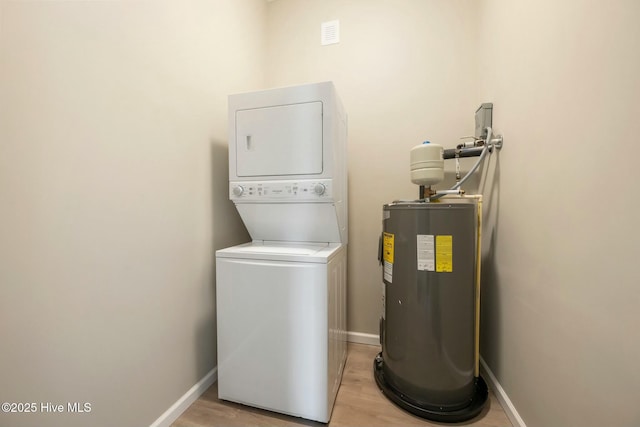 clothes washing area with laundry area, baseboards, stacked washer and clothes dryer, light wood-style flooring, and electric water heater