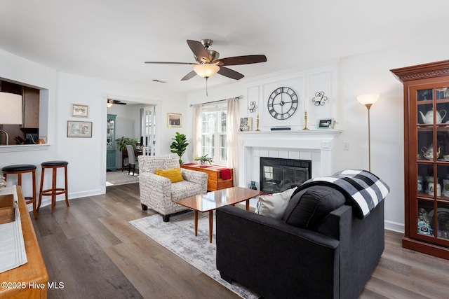 living room featuring hardwood / wood-style floors, a tiled fireplace, and ceiling fan