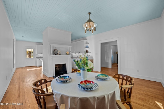 dining area featuring light wood-style flooring, a fireplace, a chandelier, and baseboards