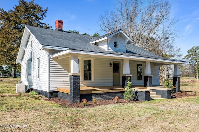 view of front of property with a front yard, covered porch, and a chimney