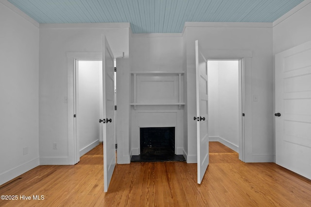 unfurnished bedroom featuring wood ceiling, light wood-style flooring, baseboards, and a fireplace with raised hearth