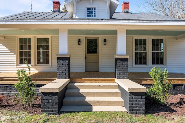 doorway to property with a porch, a standing seam roof, metal roof, and a chimney