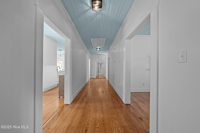 corridor featuring attic access, crown molding, light wood-style flooring, and baseboards