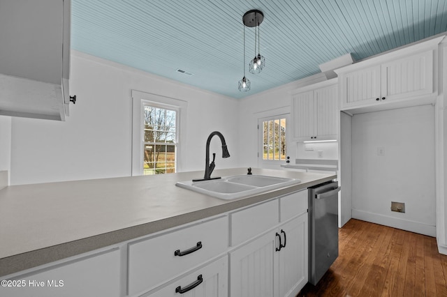 kitchen featuring decorative light fixtures, light countertops, stainless steel dishwasher, white cabinetry, and a sink