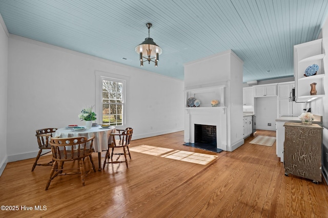 dining space featuring a fireplace with raised hearth, a notable chandelier, light wood-style flooring, and baseboards