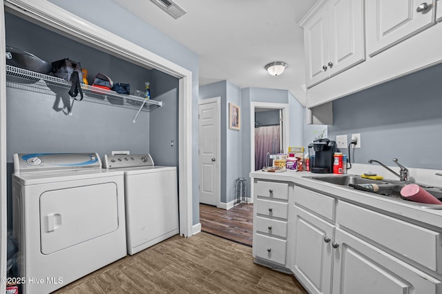 clothes washing area with visible vents, washing machine and dryer, a sink, wood finished floors, and laundry area