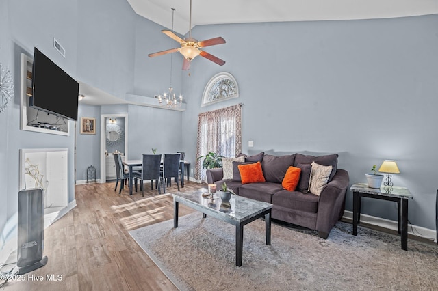 living area with high vaulted ceiling, ceiling fan with notable chandelier, wood finished floors, visible vents, and baseboards