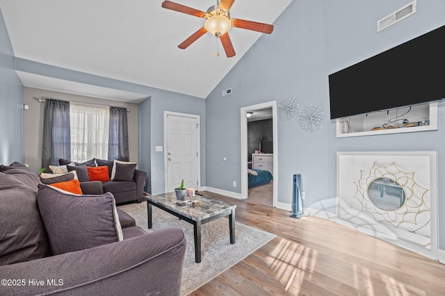 living area with light wood finished floors, visible vents, a ceiling fan, high vaulted ceiling, and baseboards