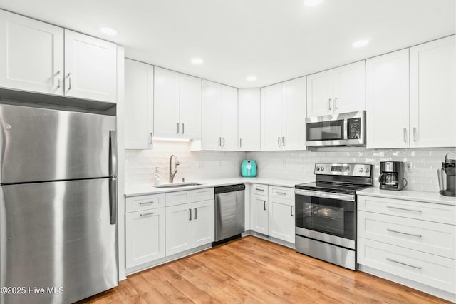 kitchen with a sink, white cabinets, light countertops, appliances with stainless steel finishes, and light wood finished floors