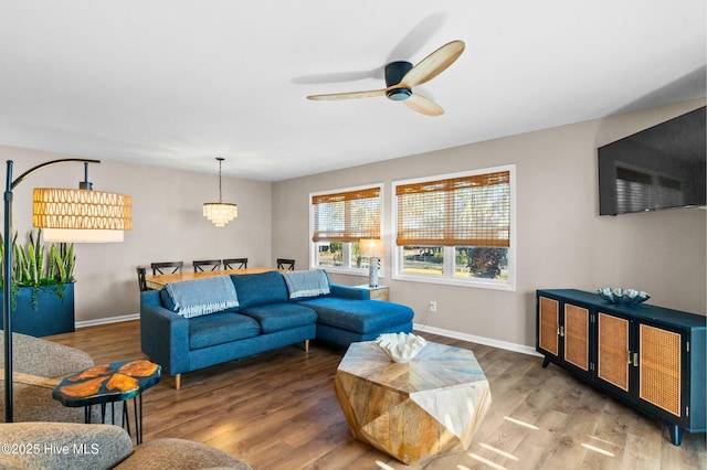 living room featuring ceiling fan with notable chandelier, baseboards, and wood finished floors