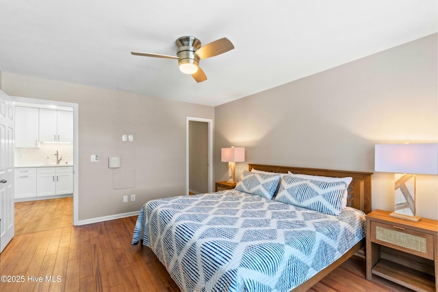 bedroom featuring light wood-style floors, a sink, ceiling fan, ensuite bath, and baseboards