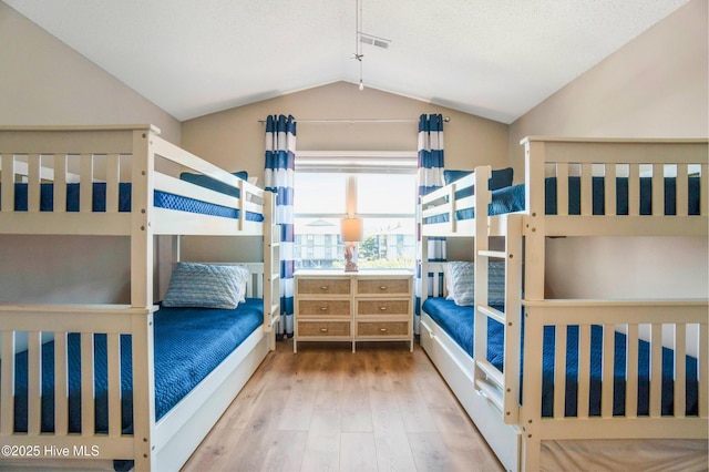 bedroom with a textured ceiling, visible vents, vaulted ceiling, and wood finished floors