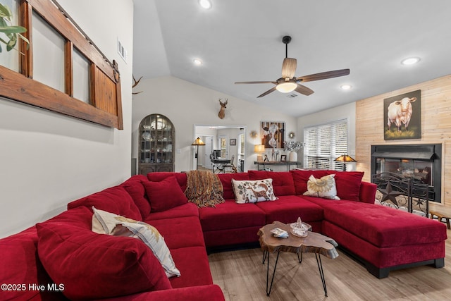 living area featuring a fireplace, wood finished floors, visible vents, a ceiling fan, and vaulted ceiling