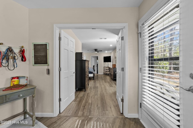 hallway featuring visible vents, light wood-style flooring, and baseboards