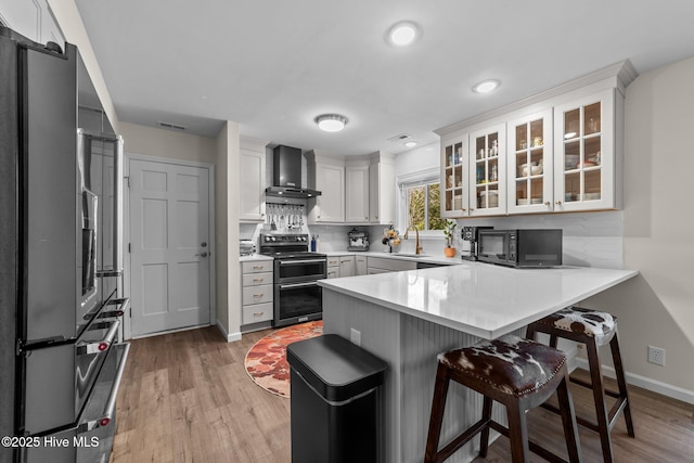 kitchen with light countertops, wall chimney range hood, freestanding refrigerator, double oven range, and glass insert cabinets