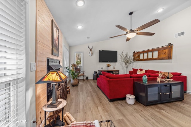 living area featuring light wood-type flooring, visible vents, vaulted ceiling, and a glass covered fireplace