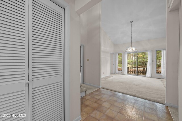 hallway featuring baseboards, high vaulted ceiling, carpet flooring, and an inviting chandelier