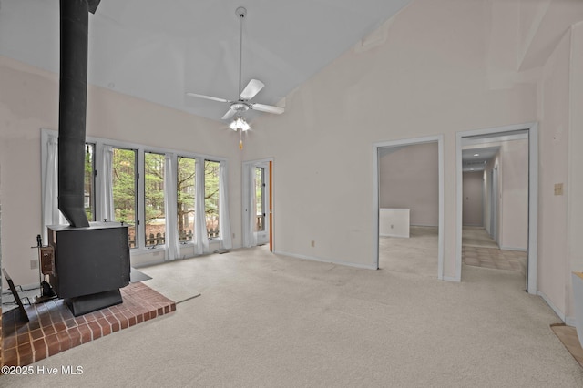 unfurnished living room featuring a wood stove, carpet flooring, high vaulted ceiling, baseboards, and ceiling fan